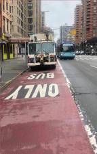 Vehicles such as this NYC Sanitation truck frequently park in the curbside bus lane on Second Ave., forcing buses to veer into regular traffic lanes. A new DOT plan will “offset” the dedicated bus lane away from the curb.