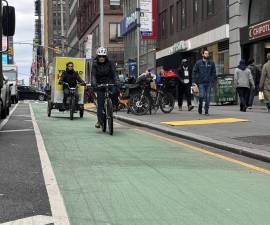 Two riders approach the intersection of Seventh Avenue and 38th Street in Midtown Manhattan. The wider, protected bike lanes are meant to make riding safer for the growing number of e-bikers. But some worry the faster, wider lanes will increase the danger to pedestrians since many bikers ignore all traffic laws.