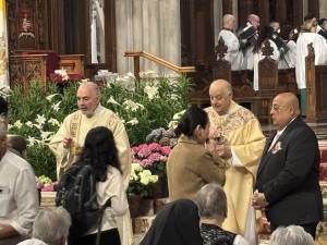 Msgr. Joseph LaMorte (gold vestments, right), giving out communion at St. Patrick’s Cathedral, said Cardinal Dolan will be back in NYC next week and will tell what he can about the conclave that elected Pope Leo XIV.