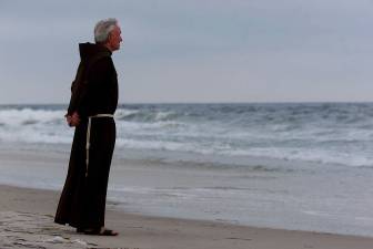 In this July 17, 2000, Father Mychal Judge, a chaplain with the FDNY stands at the shore of the Atlantic Ocean at Smith Point Park in Shirley, N.Y. before a service where 230 candles were lit for the July 17, 1996 victims of TWA Flight 800.