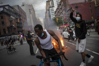 Protesters march down the street as trash burns in the background during a solidarity rally for George Floyd, Saturday, May 30, 2020, in New York. Protests were held throughout the city over the death of Floyd, a black man who died after being restrained by Minneapolis police officers on May 25.