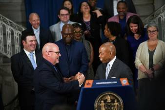 Mayor Eric Adams (at lectern) and UFT president Michael Mulgrew clasp hands after reaching a new tentative five year pact between the city and the teacher’s union. Photo: Mayors Photography Office