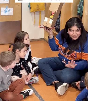 Teacher in Knicks sweatshirt explains a project to kids.