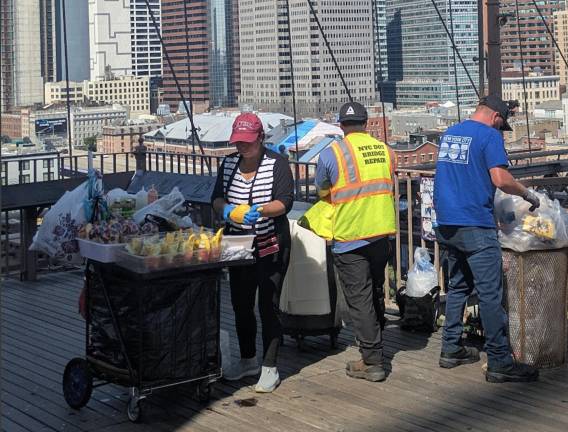 Brooklyn Bridge vendor ignoring the NO VENDING signs while DOT workers clean up behind her.