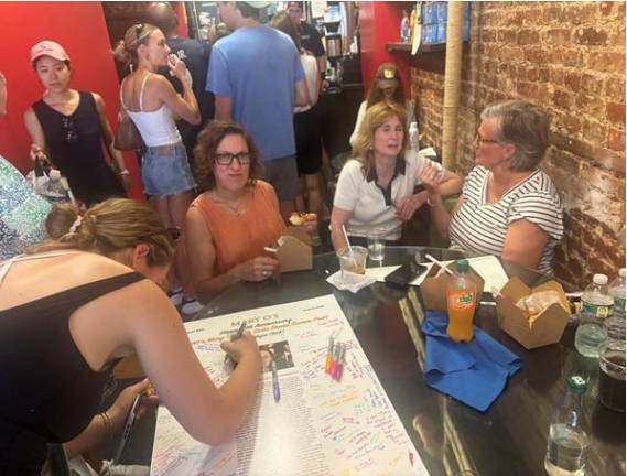Friends of Mary O’Halloran (from right to left) Tami Ellen McLaughlin, Lori Goldberg and Shelley Ann Quilly hand out sharpies to waiting customers that featured a story that appeared in the neighborhood blog Humans of New York that first ignited the social media frenzy that catapulted Mary O’s to national fame.