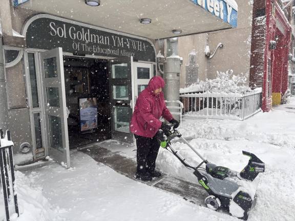 The YMHA on E. 14th St. was closed on Feb. 23, but a woman works a snowblower to clear a path for reopening on Feb. 24.
