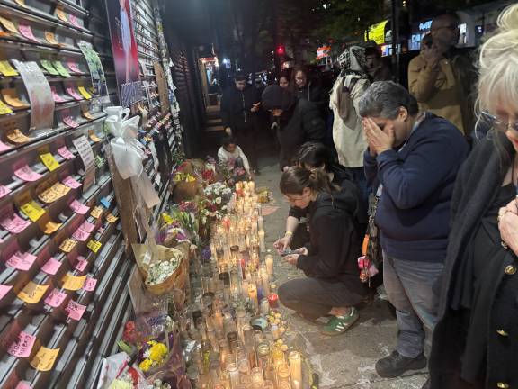 An anguished mourner holds his head in his hands at the growing memorial outside Sal’s Deli while two others knelling on the ground pen messages to the beloved bodega worker.