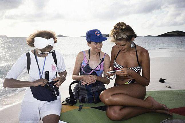Model Judit Masco looks at a polaroid during a Sports Illustrated Swimsuit Issue shoot on Palm Island in Saint Vincent and the Grenadines in the fall of 1989. Jule Campbell loads film into her camera as Jule's assistant Christine Walker looks on.