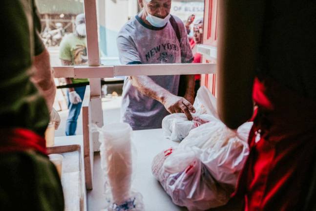 Homeless and food insecure people collect pre-packaged meals from the window at the Bowery Mission. Photo: Gabe Desanti