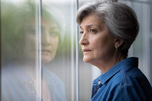 Close up thoughtful upset mature woman looking out window