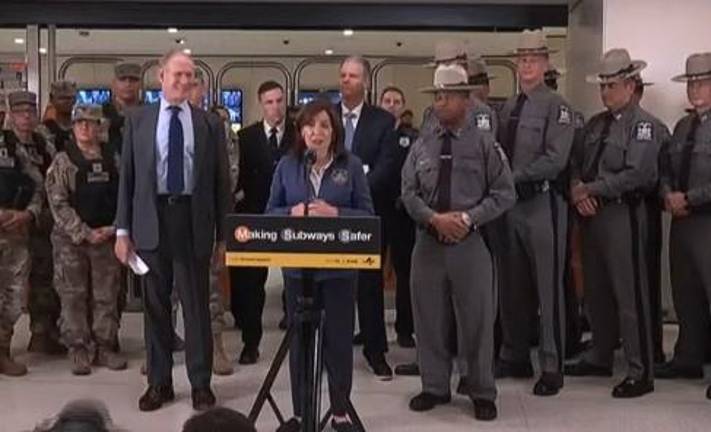 Gov. Kathy Hochul (at mic) and MTA Chairman Janno Lieber (left) say crime is down on subways and committed an additional $77 million in the new budget to keep two NYPD officers on all-night subway trains.