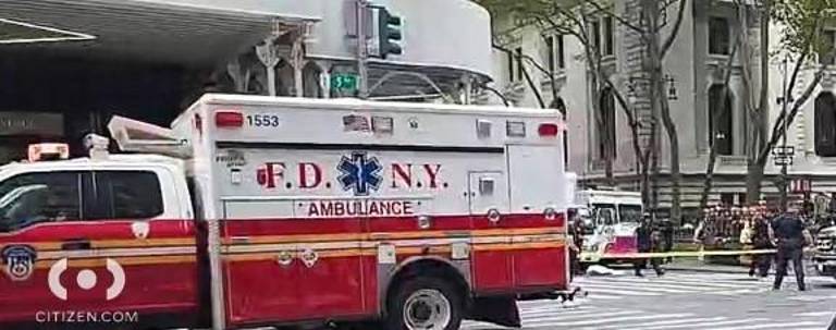 What appears to be a body covered with a sheet can be seen in the background in front of a red-and-white truck. Police said a 50-year-old woman was killed when she was struck by a vehicle near Bryant Park. A 55-year-old man, also struck, was transported to Bellevue Hospital. The driver fled the scene.