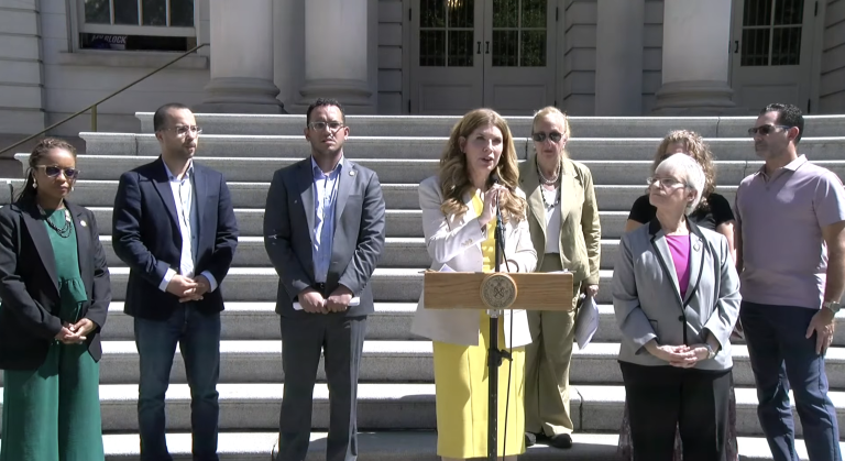 NYC Council Members on the steps of city hall, announcing a Sept. 30 hearing on e-bike safety. From left to right: Council Members Selvena Brooks-Powers, Oswald Feliz, Majority Leader Shaun Abreu, Speaker Julie Menin, Gale Brewer, and Lynn Schulman. Council Members were joined by Jessica Solano, who’s been caring for her sister after she was severely injured by an e-bike while jogging, and Solano’s husband, Brian (right).