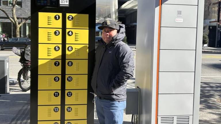 A delivery worker, who wanted to remain unnamed, swapping out batteries with Popwheels (black and yellow locker) (left), next to Swobbee (orange and grey locker) (right) on March 11 at Cooper Square in the East Village. Photo Credit: Alessia Girardin.